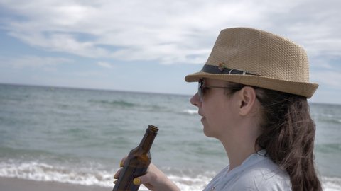 Portrait of a woman in sunglasses drinking beer from a bottle by the sea
