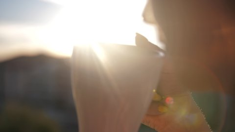 woman drinking coffee on the balcony admiring the sunset, close up