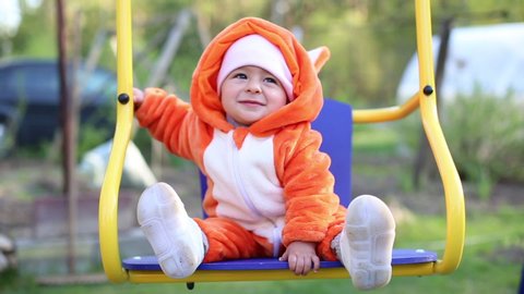 Happy little baby infant swinging on a swing. The girl is dressed in a cosplay fox costume. Pajamas called kigurumi.