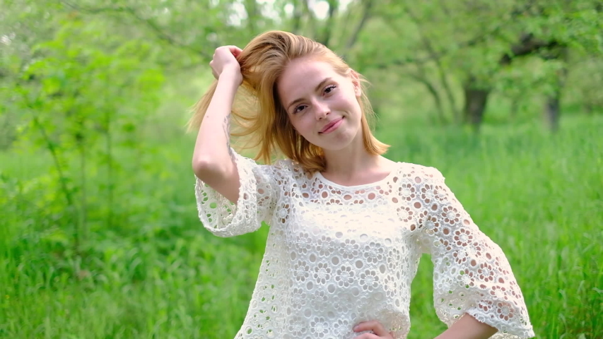 Beautiful attractive young woman posing in spring park wearing white knitted top and blue jeans, slow motion	

