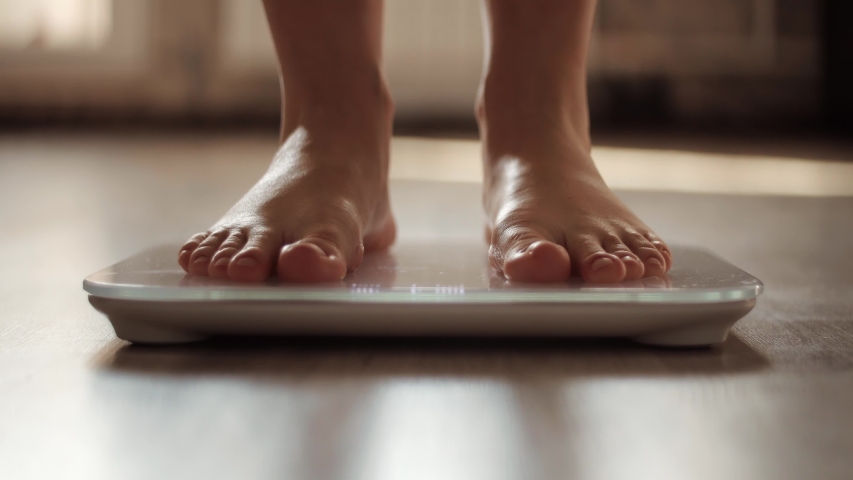 Woman On Scales Measure Weight. Girl Legs Step Bathroom Scale. Fitness Diet Woman Feet Standing Weighing Scales On Room. Female Dieting Checking BMI Weight Loss. Barefoot Measuring Body Fat Overweight