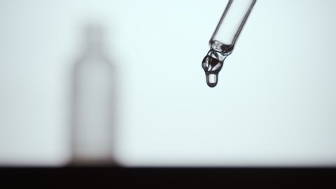 Monochrome shot of Liquid dropper or pipette. Drop of clear thick fluid falling on white background. Eyedropper squeezing out meds droplets. Slowmotion
