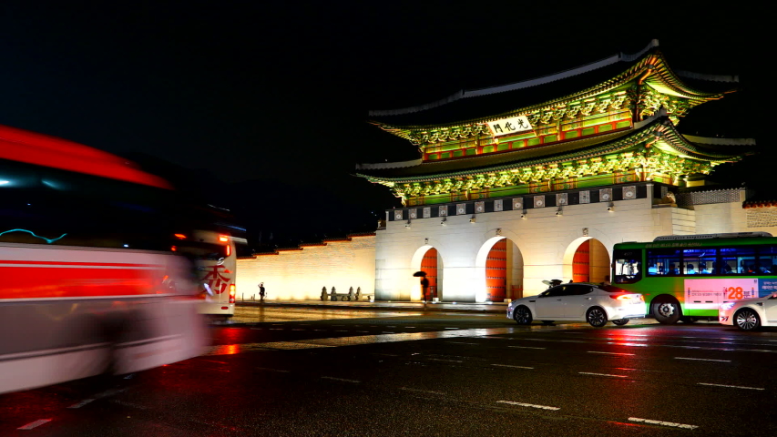 Seoul / South Korea - 01 01 2019: Circa - Night time lapse of busy traffic passing in front of Gyeongbokgung Palace in South Korea, illuminated oriental building.