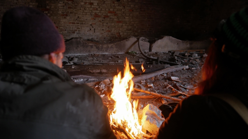 man and a woman are sitting near a fire in an underground shelter