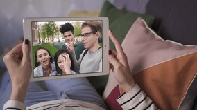 girl lying on sofa greeting and talking to her four friends video call on tablet. waving hand. facetime, internet, skype, online, long distance, chatting concept