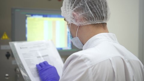 Man employee work with document and computer in interior of pharmaceutical plant. American male worker holding paper in hand and watching pc screen while working in pharma medical company. Concept