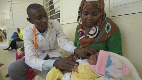 Doctor examining baby in busy clinic.
