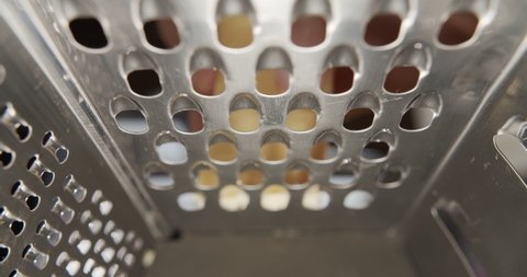Frame inside metal grater. Close-up grated cheese on metal grater in slow motion