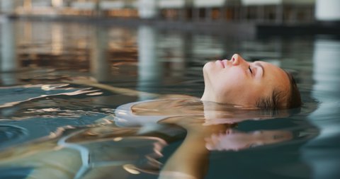 Close up of an young woman is enjoying and having relax in an indoor illuminated with night lights swimming pool in a luxury wellness center.