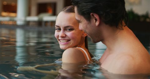 An young happy couple is enjoying and having relax in a indoor swimming pool in a luxury wellness center.