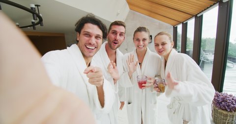 The young happy couples in white bathrobes are making a selfie or a video call after various treatments in a luxury wellness center.