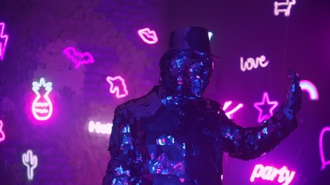 A man dances in neon light in a glass suit. Shiny sparkling silver suit, and blue purple neon light. New year party.