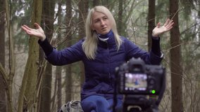 European blonde woman writes blog as a blogger sitting in forest, park. dslr
