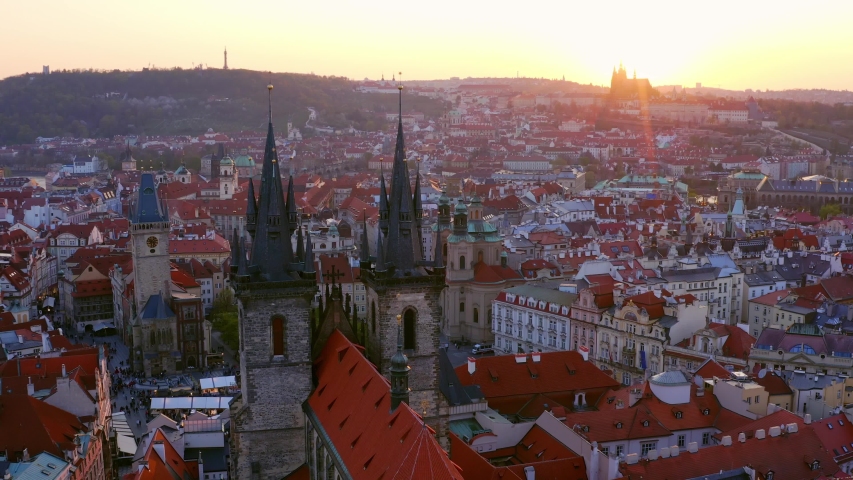 Overall view from high Church of Our Lady and old town district in Prague at sunrise. Drone flying forwards to steeples of cathedral in sun shining moving at low above typical Czech buildings 
