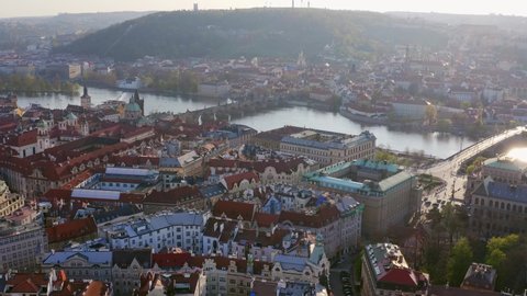 Aerial footage over Prague and old town district at daytime. Drone flying forwards over red tiled roofs of typical Czech buildings to Vltava river on horizon. Bird eye old European city in sunny day