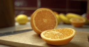 
Focus movement on a juicy orange. Sliced ​​fruit on a cutting board in the kitchen. Bananas and lemons on the background. Yellow-orange color.