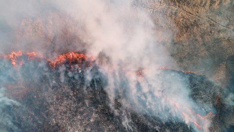 Strong fire in an empty field. Strong smoke from the burning place. View from a height, vertically from top to bottom, smooth rise up. Dry grass burns, natural disaster. Aerial view.