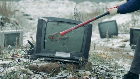 A person smashes old TV with a hammer at a landfill. Man crashes old TV set.