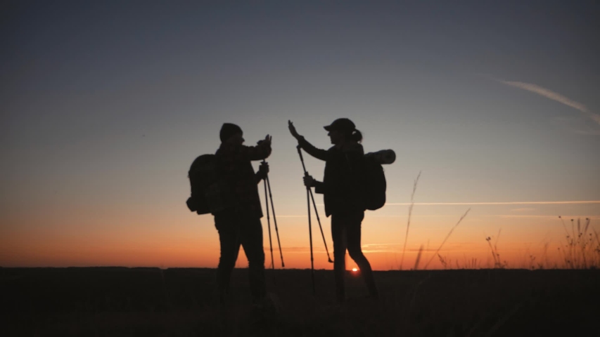 Silhouettes of two hikers with backpacks enjoying sunset view from top of a mountain. Enjoying the sunset view from mountain top above the clouds. Happy couple winner mountain top concept. | Shutterstock HD Video #1041793351