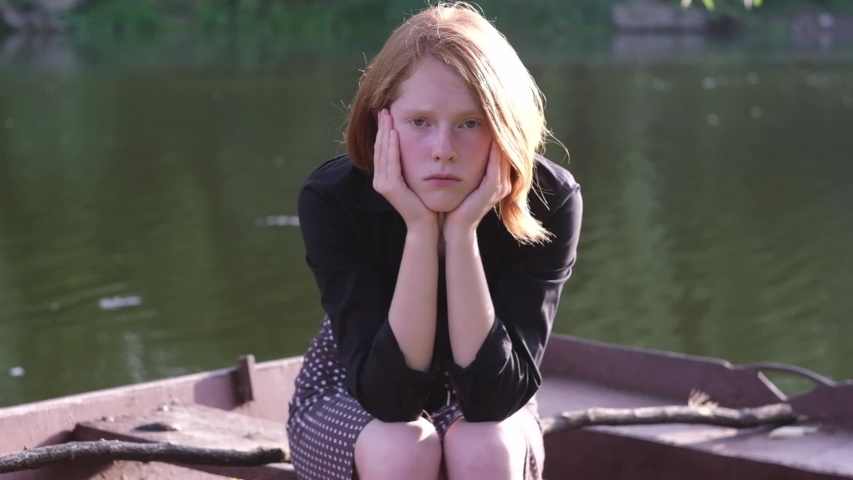 Beautiful ginger girl sitting sad in a rusty boat. Butterfly nearby fly away