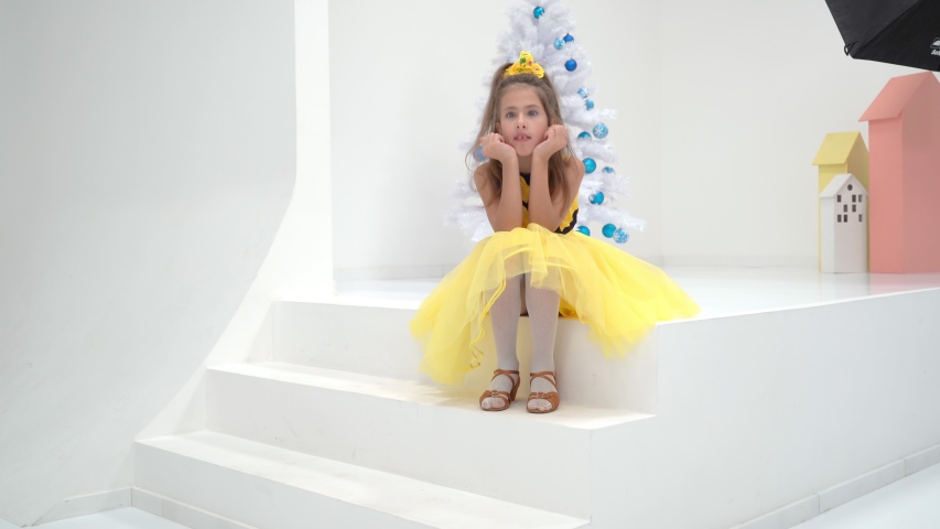 Little girl sitting on a white staircase near the Christmas tree