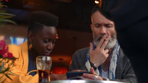 Gorgeous African Business Woman Shows Her Older Male Caucasian Partner Something on a Tablet Computer Device. Interracial Business Partners Meet Offsite at a Sports Bar in Paris. Portrait, slow-motion
