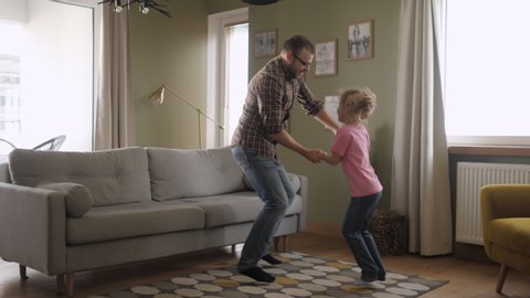 Young Father and Her Daughter Playing in Living Room. Funny Happy Family Father and Daughter are Dancing hold hands and jump at Home. Love Lifestyle Home. Slow Motion.