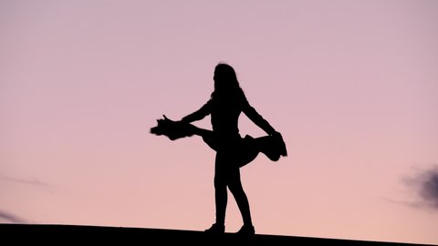 Cheerful young woman turn around, hold scarf in hands stretched out, black silhouette against pink sunset sky. Happy person dance, whirl round on place