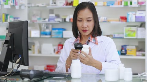 asian women Pharmacist scanning barcode white medicine bottle on to the computer in pharmacy store Thailand footage 4k video  , videoclip de stoc