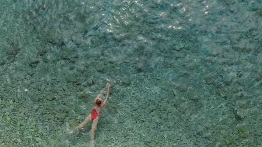 Aerial view of young woman swimming breaststroke in crystal clear ocean. She is relaxed and she loves water.
