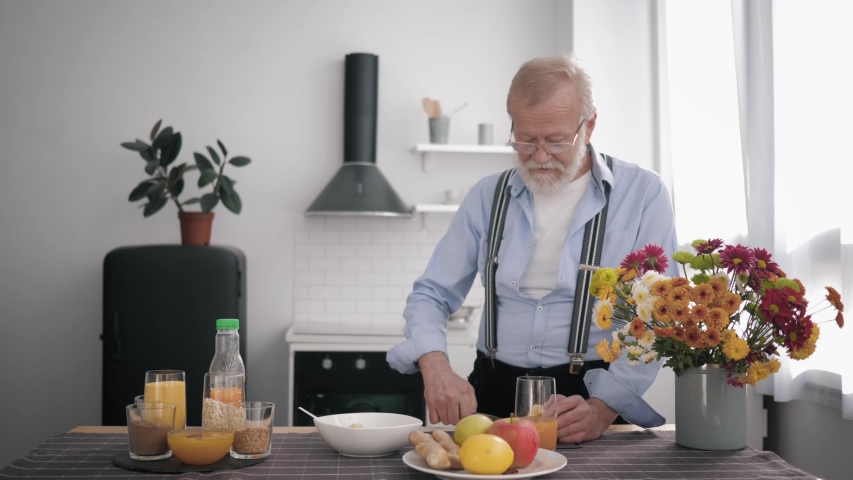 grandparent, caring grandfather with a beard and glasses for vision prepares vitamin food for himself and his smiling granddaughter standing at the table