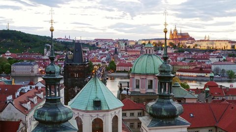Aerial footage old town district in Prague at twilight. Cityscape from high, drone flying at low above red tiled roof of buildings in downtown. View illuminated and river at evening 