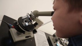 White little 9 years old kid looking through microscope at tiny object. Real time full hd video footage.