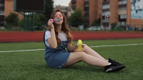 Beautiful young woman in sunglasses blowing soap bubbles outdoors and spinning around. Close view. Slow motion. girl in trendy orange sunglasses