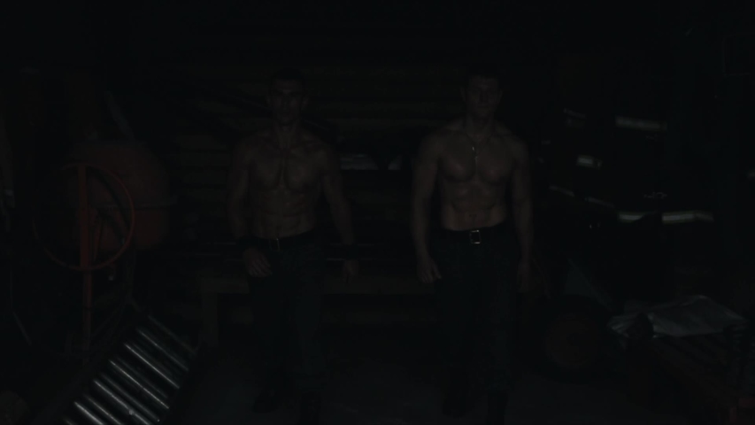Two strong confident topless men walking towards the camera in the dark building. Slow motion