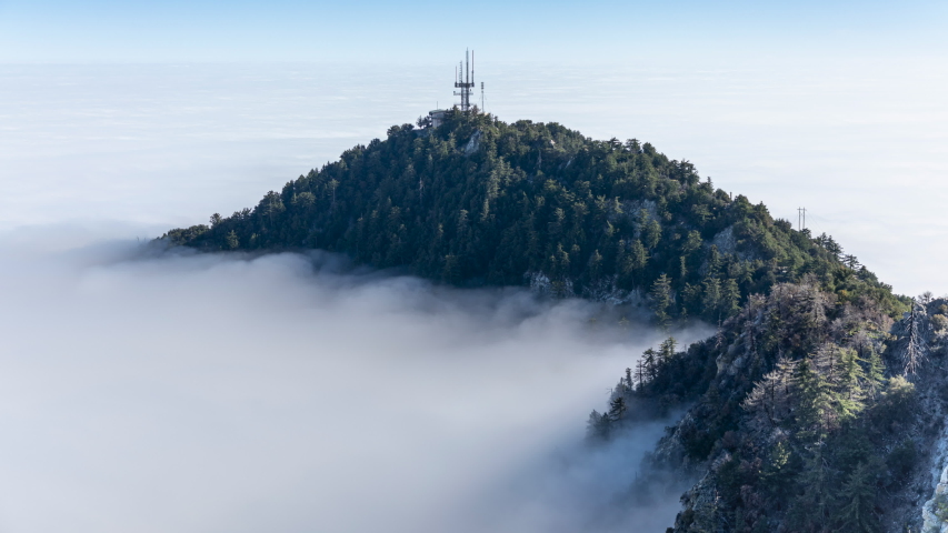 Dense fog surrounds a hilltop in San Gabriel Mountains. Time lapse video. A forest-covered peak looks like a green island in the middle of a white sea of ​​clouds. Angeles National Forest. 4K