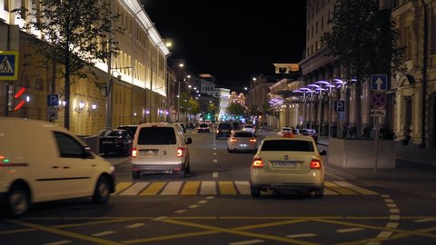 MOSCOW - CIRCA OCTOBER 2019: View of a busy city street. Night. Heavy traffic. Bright, colorful and illuminated building facades. Parked cars. Pedestrians cross the road. Ultra HD