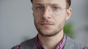 Head and shoulders closeup video portrait of intelligent serious young man in eyeglasses and with beard on his face looking at camera