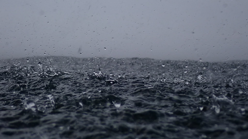 Rain drops into the endless ocean, close up. It briefly bounces back to the air after it hits the sea surface, slow motion.