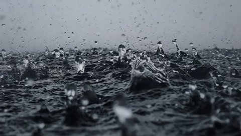 Rain drops into the endless ocean, close up. It briefly bounces back to the air after it hits the sea surface, slow motion.
