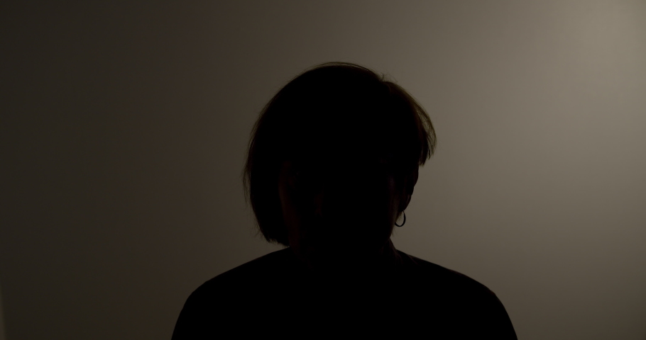 Silhouette of a woman giving an anonymous interview in a dark room. Royalty-Free Stock Footage #1041869833