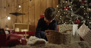 Boy playing with christmas gifts and toys close christmas tree in rustic room chalet 4k footage