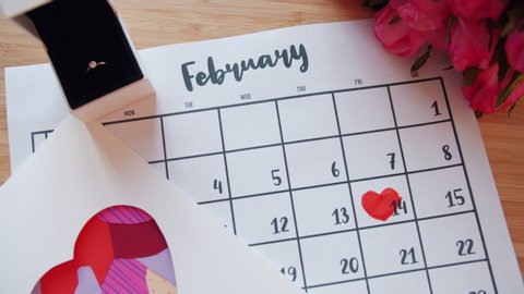 Valentine's day attributes are displayed on table - calendar with heart shape around February 14, bunch of flowers and ring in gift box. Holidays and events concept.