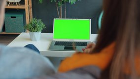 Happy couple man and woman are looking at green chroma key laptop screen holding hands at home enjoying video together. People and technology concept.