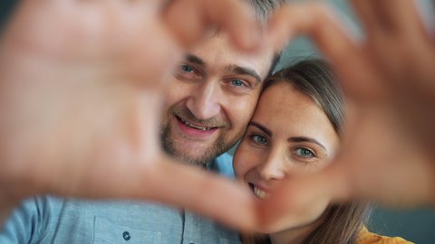 Portrait of happy couple showing heart shape with hands smiling looking at camera standing in apartment together. People, relations and feelings concept.