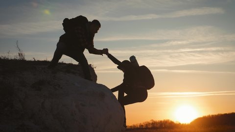 Silhouette of helping hand between two climber. two hikers on top of the mountain, a man helps a woman to climb a sheer stone. couple hiking help each other silhouette in mountains with sunlight.