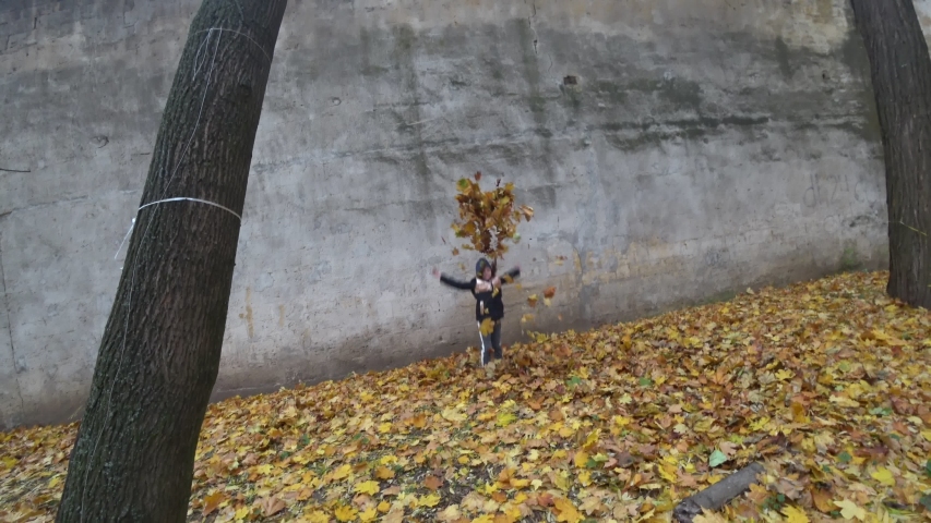 Little girl is playing with leaves in the autumn park