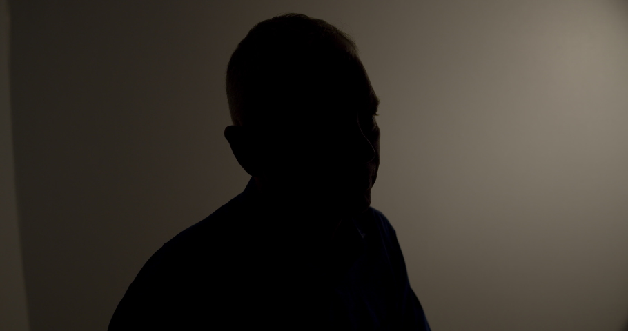Witness anonymous man being interviewed in a dark room silhouette lateral Royalty-Free Stock Footage #1041892339