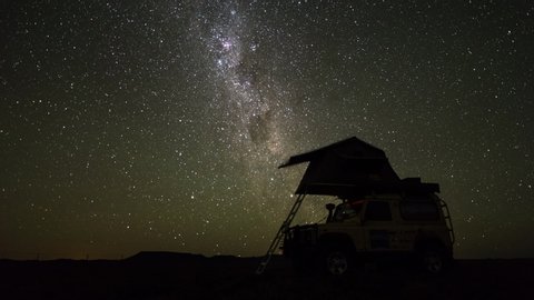 A slow linear night timelapse of a safari vehicle (4x4) in an adventurous wild camping location with a rooftop tent against the Milky Way and starry sky. 4K