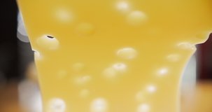 Close-up of slice of cheese with holes falling on the board. Slow motion video 4K
